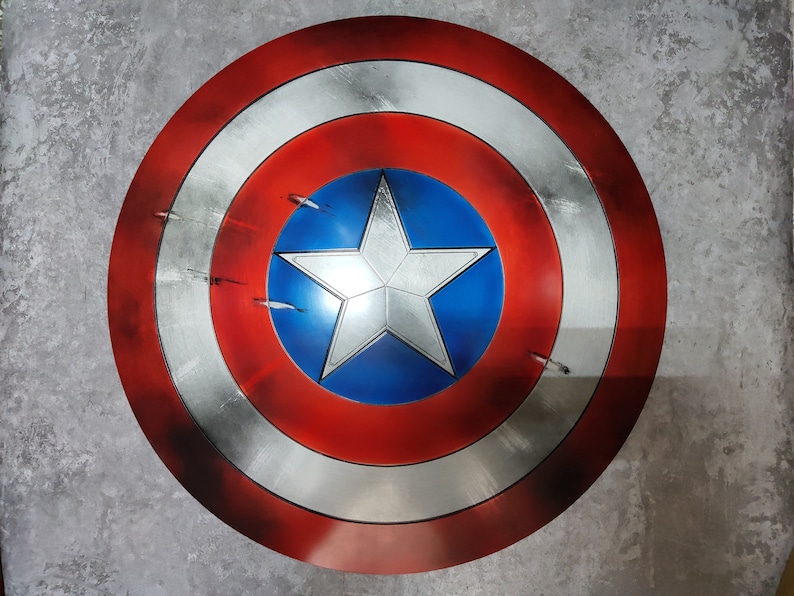 May include: A red, white, and blue Captain America shield with a five-pointed star in the center. The shield has a circular design with concentric circles.