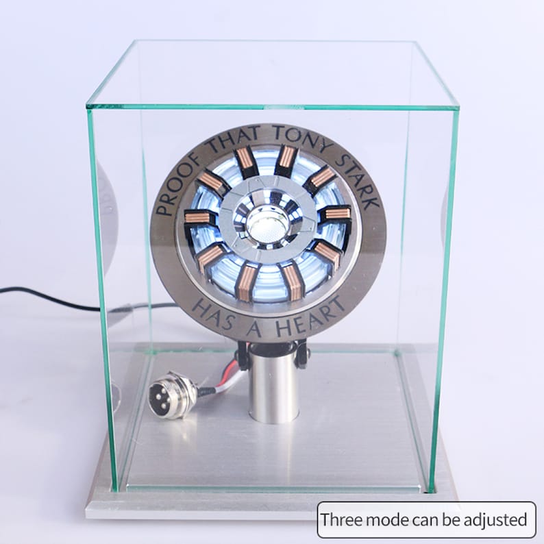 May include: A silver and copper-colored Iron Man Arc Reactor replica with a clear light in the center. The replica is in a glass display case with the text "Proof that Tony Stark has a heart" around the edge.