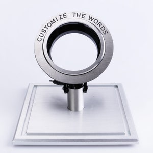 May include: A silver ring with the words "Customize the Words" engraved around the outside. The ring is on a silver stand.