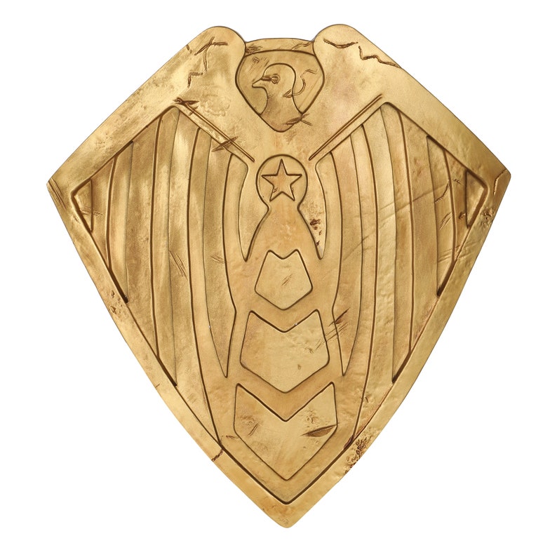 May include: A gold shield with an eagle and star design. The shield has a distressed, aged look.