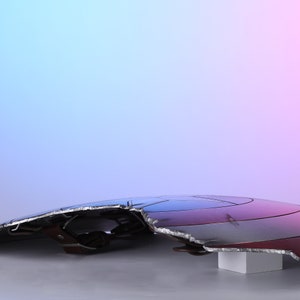 May include: A distressed, metallic shield with a red, white, and blue color scheme. The shield has a jagged edge and is resting on a white block. The background gradient transitions from blue to pink.