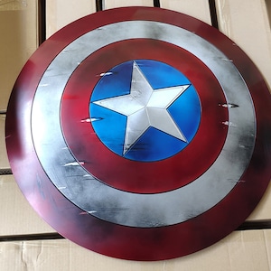 May include: A red, white, and blue Captain America shield with a distressed, weathered look. The shield has a large white star on a blue background.