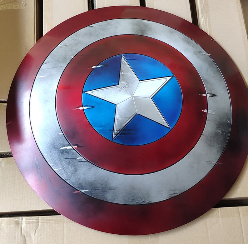 May include: A red, white, and blue Captain America shield with a distressed, weathered look. The shield has a large white star on a blue background.