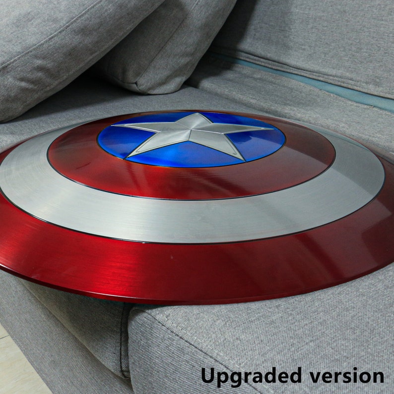 May include: A red, white, and blue Captain America shield with a silver rim. The shield is made of metal and has a shiny finish. The shield is sitting on a gray couch.