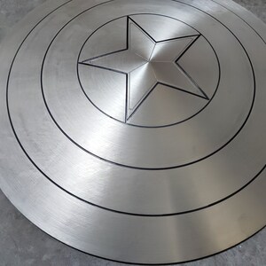 May include: A silver metal shield with a five-pointed star in the center. The shield has concentric circles around the star.