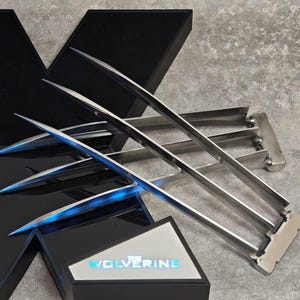Peut inclure: Ensemble de griffes Wolverine en métal argenté avec des lames pointues et tranchantes. Les griffes sont présentées avec un logo en forme de X noir et argent et une boîte noire avec le texte "Wolverine".