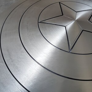 May include: A silver metal shield with a black star in the center. The shield has concentric circles around the star.