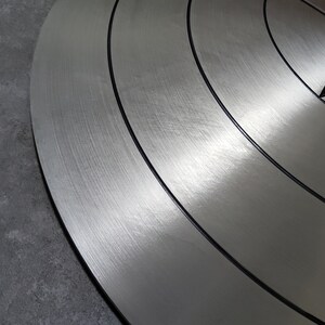 May include: A close-up of a silver metal shield with a brushed finish and black concentric circles. The shield has a star-shaped design in the center.