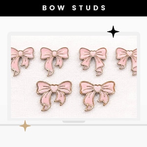 May include: Six light pink enamel bow studs with gold-toned metal outlines. Each bow features a small heart detail at the centre knot. The text BOW STUDS is displayed in white capital letters against a black rectangular header at the top.
