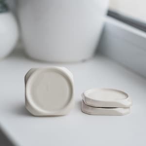 Könnte beinhalten: Drei weiße Untersetzer aus Keramik mit geometrischem Design. Die Untersetzer sind übereinander gestapelt.