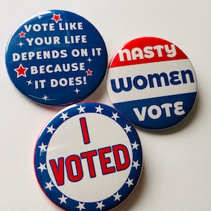 May include: Three round political buttons with text. One button says "VOTE LIKE YOUR LIFE DEPENDS ON IT BECAUSE IT DOES!" in white on a blue background. Another says "NASTY WOMEN VOTE" in red, white, and blue. The third says "I VOTED" in red.