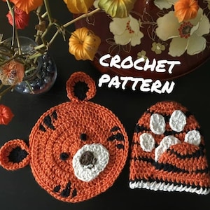 May include: Crochet pattern for a tiger hat and matching tiger paw applique. The hat is orange and black with white paw prints. The applique is orange and black with a white face.