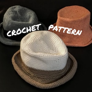 May include: Three crocheted hats in different colors: gray, peach, and white with brown trim. The hats are all the same style, with a wide brim and a crown that is slightly taller than the brim. The hats are arranged in a row, with the gray hat on the left, the peach hat in the middle, and the white hat on the right. The text "CROCHET PATTERN" is written across the image.