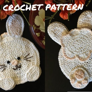 Könnte beinhalten: Ein gehäkeltes weißes Kaninchen mit rosa Ohren und Füßen. Das Kaninchen hat eine schwarze Nase und braune Schnurrhaare. Das Kaninchen sitzt auf einer schwarzen Oberfläche.