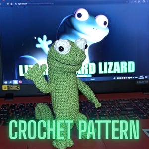 May include: A handmade green crochet lizard with white accents, posed in front of a laptop screen displaying a lizard graphic. The words "CROCHET PATTERN" are displayed in a green font at the bottom of the image.