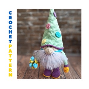 May include: A crocheted gnome with a green hat with colorful polka dots, a purple beard, and a bouquet of blue flowers. The gnome is standing on a wooden surface.