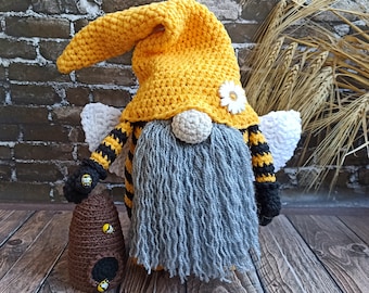 May include: A handmade crochet gnome with a yellow hat, gray beard, and bee-themed accents. The gnome has black and yellow striped arms and wings, and holds a brown beehive with yellow bee embellishments. A white daisy decorates the hat.