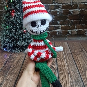 Puede incluir: Un mu&ntilde;eco de elfo de Navidad de crochet con un gorro a rayas blanco y rojo, una bufanda verde y pantalones a rayas verdes y negros.