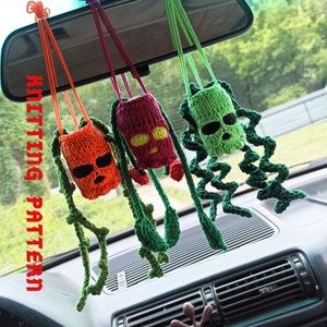 May include: Four crocheted hanging ornaments in the shape of a skull with different coloured bodies. The ornaments are hanging from a rearview mirror in a car. The ornaments are green, orange, red, and green.
