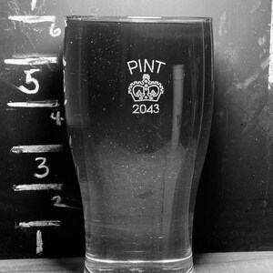 May include: A clear glass pint glass with a crown and the text "PINT 2043" etched on the side.