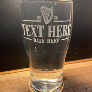 May include: A clear glass pint glass with an etched design of a harp, the numbers 20 and 25, the text "TEXT HERE" and "DATE HERE".