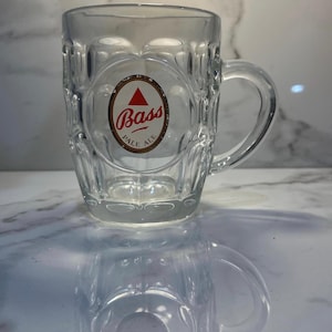 May include: Clear glass beer mug with a handle. The mug features a textured design and a circular logo with the words "Bass Pale Ale" and a red triangle.