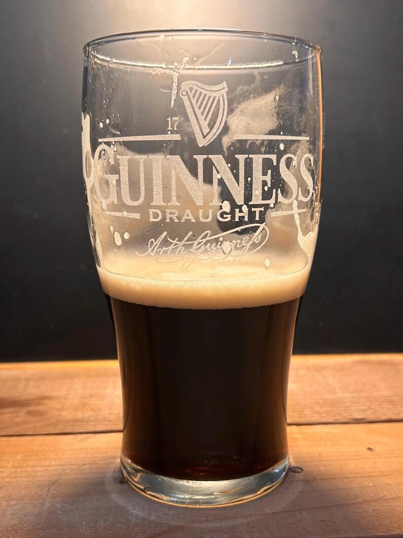 May include: A pint glass of Guinness Draught stout. The glass is etched with the Guinness logo, the words "Guinness Draught" and "Arth Guinness". The stout is a dark brown colour with a creamy, tan head.
