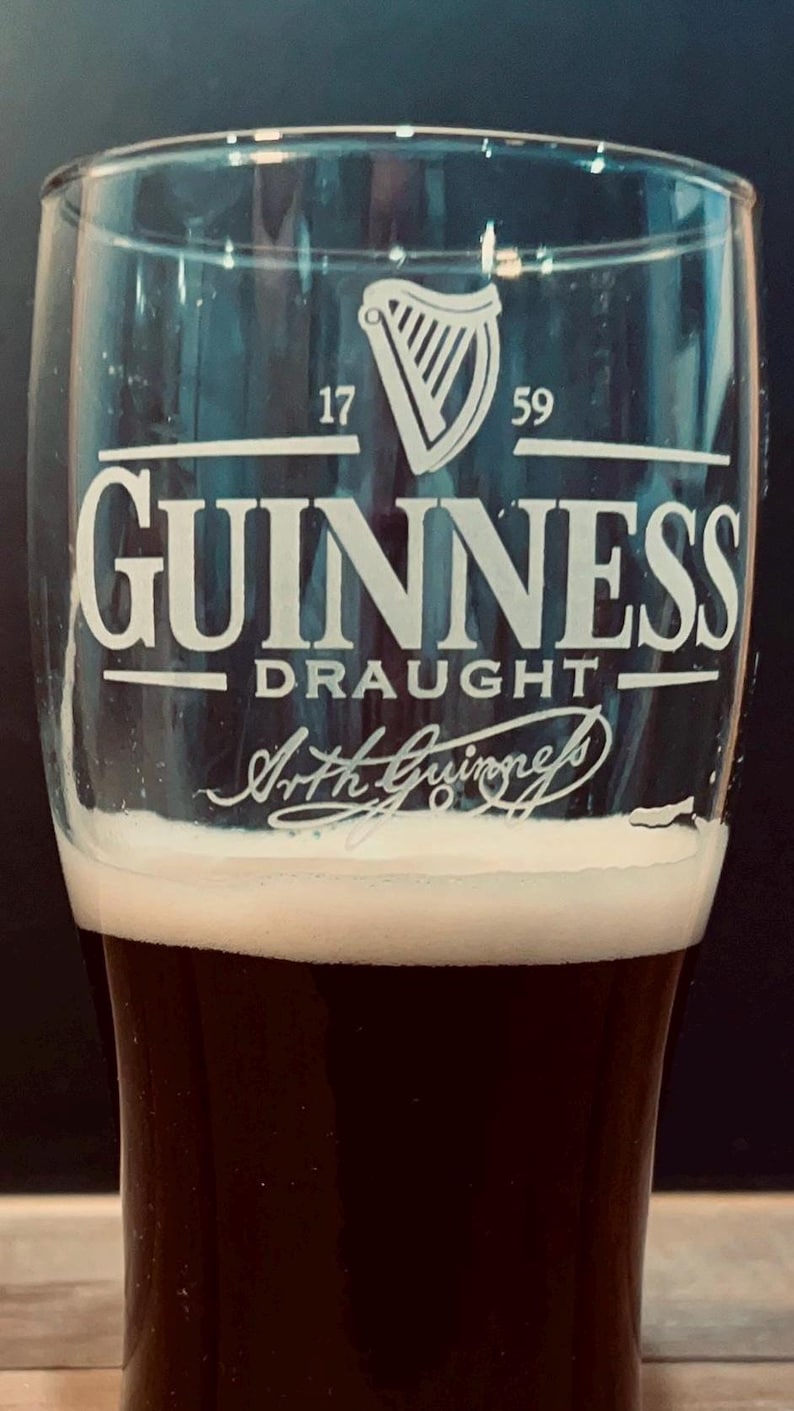 May include: A pint glass filled with dark stout, topped with a creamy white head. The glass features the Guinness logo, including a harp symbol and the words "Guinness Draught". The text "1759" is also visible.