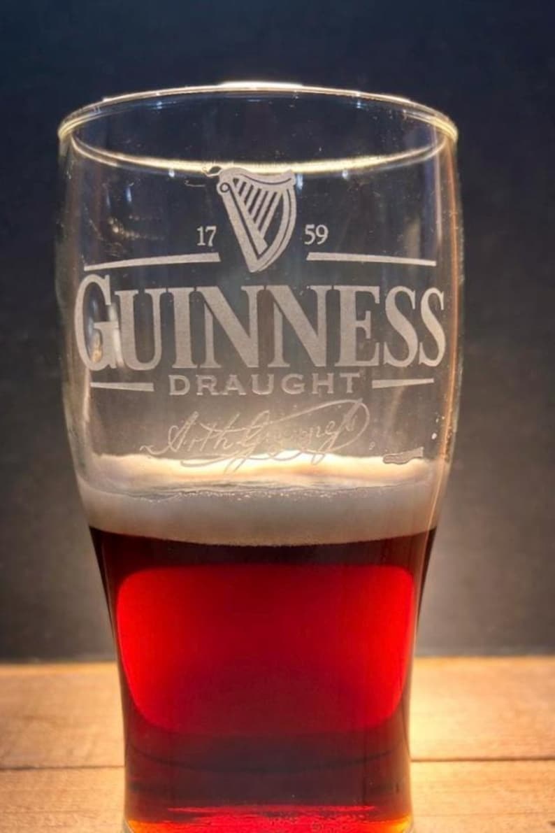 May include: A pint glass of Guinness draught beer. The glass is etched with the Guinness logo, the year 1759, and Arthur Guinness' signature. The beer is a dark red colour with a thick, creamy white head.