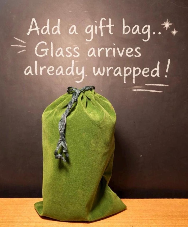 May include: A green velvet gift bag with a drawstring closure. The bag is on a dark background with the text "Add a gift bag... Glass arrives already wrapped!"