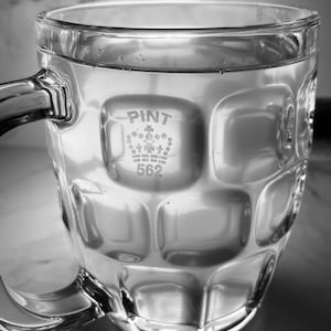 K&ouml;nnte beinhalten: Ein klares Glas-Bierglas mit einer strukturierten Oberfl&auml;che. Das Glas hat eine Krone und den Text "PINT 562" auf der Seite.