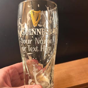 May include: A pint glass with the Guinness logo and the text "Your Name or Text Here". The glass has beer residue and foam. The Guinness logo is a gold harp.
