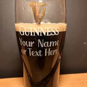May include: A pint glass filled with dark stout beer, topped with a creamy head. The glass features the Guinness logo and the text "Your Name or Text Here". The Guinness logo is a gold harp.