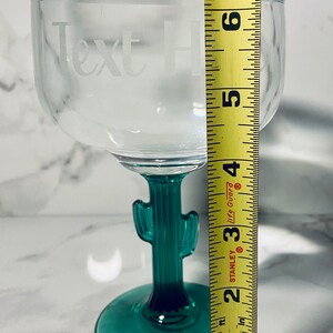May include: Clear margarita glass with a green cactus stem and base. The glass has the words "Text Here" etched on the bowl. The glass measures approximately 6 inches tall.