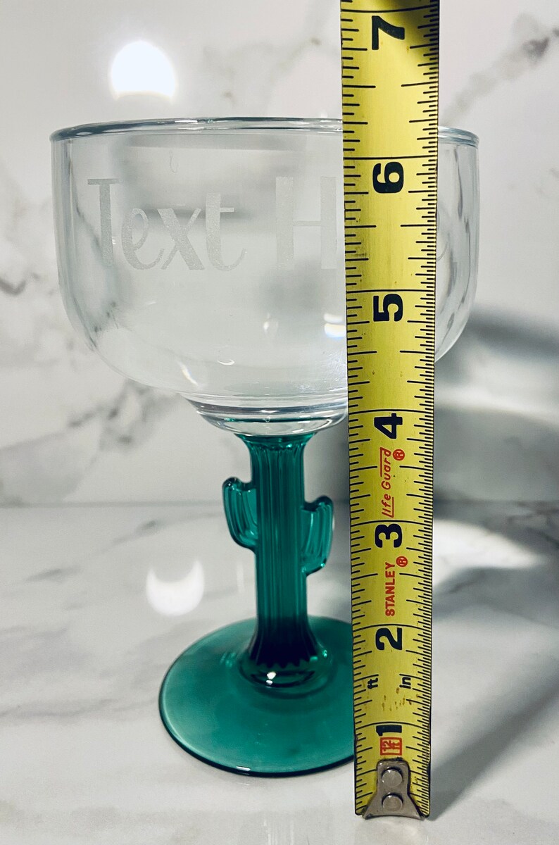 May include: Clear margarita glass with a green cactus stem and base. The glass has the words "Text Here" etched on the bowl. The glass measures approximately 6 inches tall.