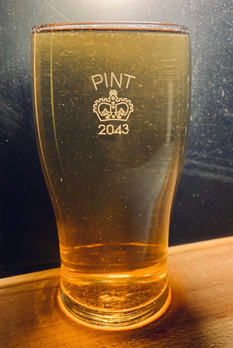 May include: A clear glass pint glass with the words "PINT" and "2043" etched on the side. A crown design is also etched on the glass.
