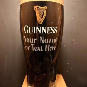 May include: A black Guinness pint glass with a creamy head. The Guinness logo and a harp are displayed in white and gold. The text "Your Name or Text Here" is below the logo, allowing for personalization.