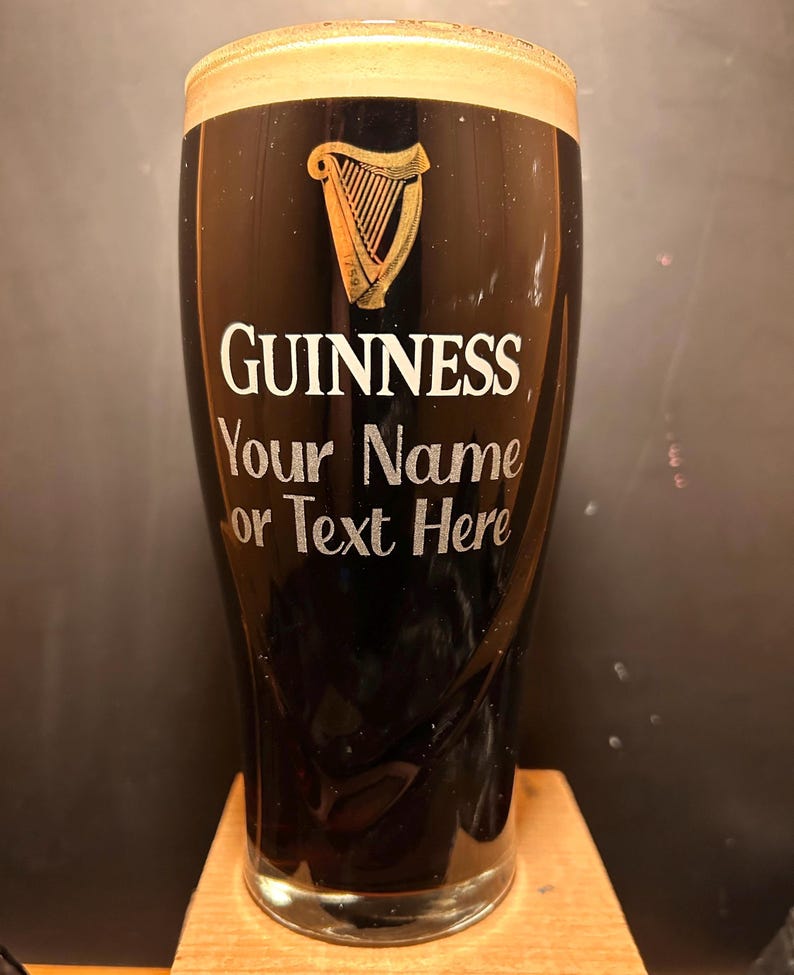 May include: A black Guinness pint glass with a creamy head. The Guinness logo and a harp are displayed in white and gold. The text "Your Name or Text Here" is below the logo, allowing for personalization.