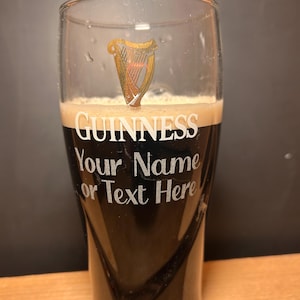 May include: A pint glass of dark stout beer, with the Guinness logo and the text "GUINNESS Your Name or Text Here". The glass has a gold harp emblem and a foamy head.