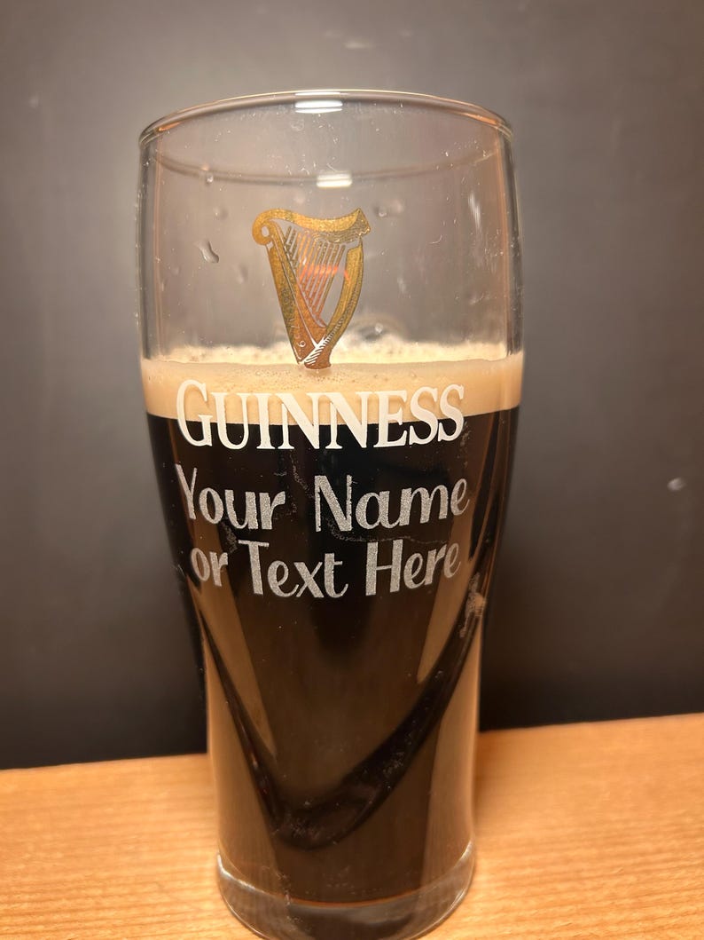 May include: A pint glass of dark stout beer, with the Guinness logo and the text "GUINNESS Your Name or Text Here". The glass has a gold harp emblem and a foamy head.