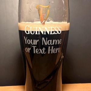 May include: A pint glass filled with dark stout beer and a creamy head. The glass features the Guinness logo and the text "Your Name or Text Here" in white lettering. A golden harp design is visible near the top.