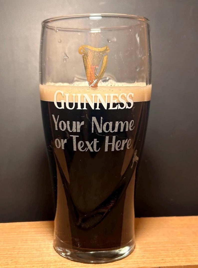 May include: A pint glass filled with dark stout beer and a creamy head. The glass features the Guinness logo and the text "Your Name or Text Here" in white lettering. A golden harp design is visible near the top.
