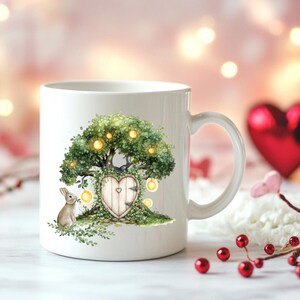 Puede incluir: Taza de cerámica blanca con una ilustración caprichosa de una casa en forma de corazón en un árbol con una puerta, rodeada de hojas verdes y luces brillantes. Un pequeño conejo está de pie cerca de la casa del árbol.