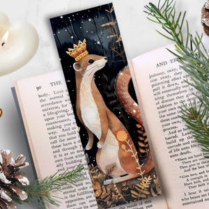 May include: A bookmark featuring a watercolor illustration of a weasel wearing a crown, standing on its hind legs in a forest setting. The background is a dark blue with white stars and a few yellow flowers.