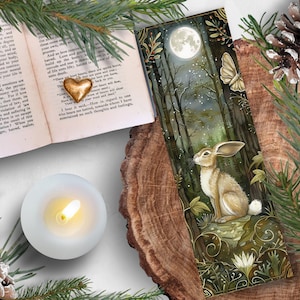 Peut inclure: Un marque-page aquarelle représentant un lapin blanc regardant une pleine lune dans un décor de forêt. Le marque-page est entouré de feuillage vert et d'un papillon.