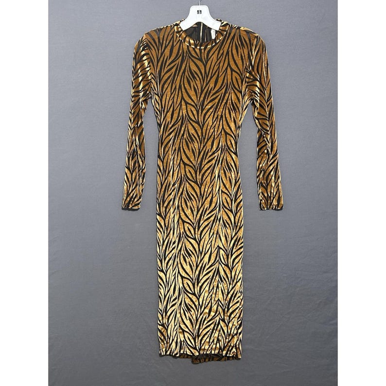 May include: A long, floor-length dress with long sleeves, featuring a gold and black leaf pattern. The dress is made of a velvet-like fabric and hangs on a white hanger against a grey background. It has a round neckline and a back zipper.