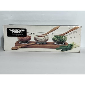 Peut inclure: Un ensemble de condiments en teck Winsome Wood de 3 pièces. L'ensemble comprend trois bols en verre transparent avec des cuillères en bois, posés sur un plateau en bois. Les bols contiennent des ingrédients rouges, blancs et verts.