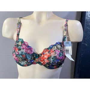 May include: A floral-patterned bra in a 34B size. The bra features a colorful design with red, pink, blue, and green flowers. The straps and edges are also patterned with floral designs. The bra is displayed on a mannequin.