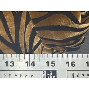 May include: Close-up of a fabric with a zebra stripe pattern. The fabric has gold and black stripes. A ruler is placed across the bottom of the fabric, with measurements in centimetres.