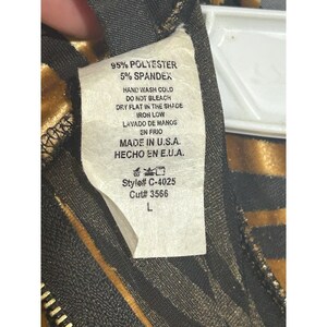 May include: A clothing label with the text "95% POLYESTER 5% SPANDEX" and washing instructions. The label also states "MADE IN U.S.A.". The label is attached to a garment with a black zipper and a gold and black pattern.